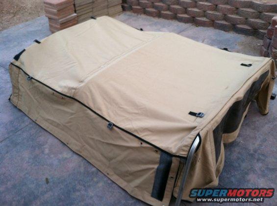 Vehicle rooftop tent folded up on a concrete surface, with brick wall in background