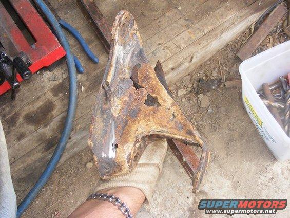 rusted metal bracket held by a gloved hand, with tools and a container of drill bits nearby