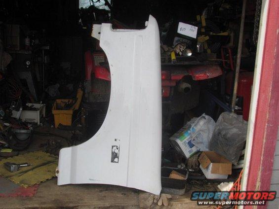 White vehicle fender leaning against a wall in a cluttered garage