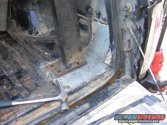 Close-up of rusty vehicle interior floor and body panel with a hammer resting on it