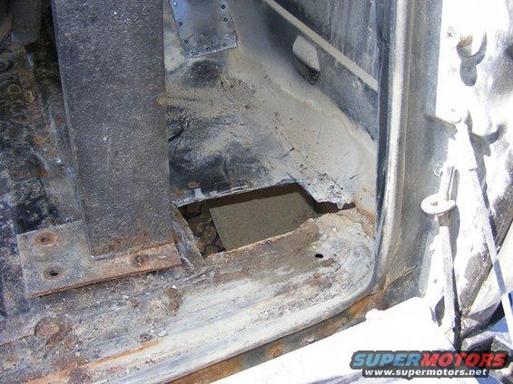Rusty vehicle floor with a hole, showing dirt and debris underneath