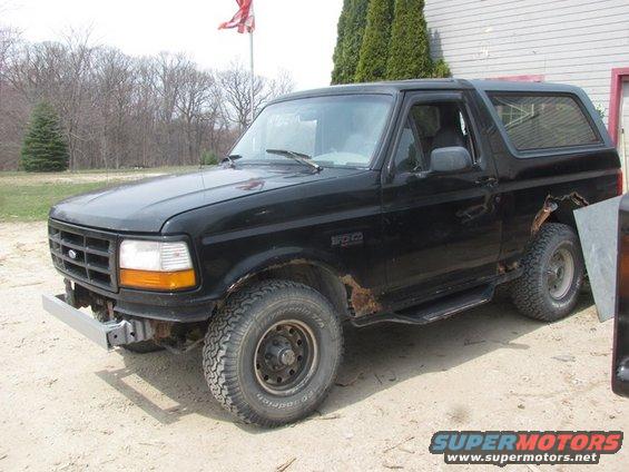 Black Ford Bronco with rust spots on the rear quarter panel and a silver aftermarket bumper