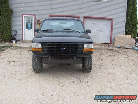 Black Ford Bronco with aftermarket wheels parked in front of a garage
