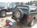 1996 Ford Bronco - Two Ford Broncos are parked outside, one black and one camouflage. The black Bronco shows rust on the rear quarter panel.