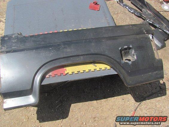Black rear fender with fuel door opening. Part is on a gray surface