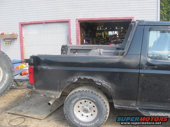 Black Ford Bronco side view, showing significant rust damage on rear wheel well. A spare tire is visible on the left