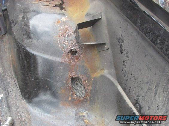 rusted out section of a vehicle's floor pan with a metal bracket attached