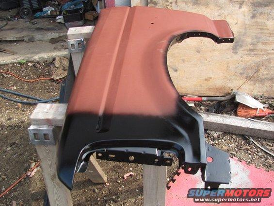 Red and black car fender on sawhorses, showing primer and paint