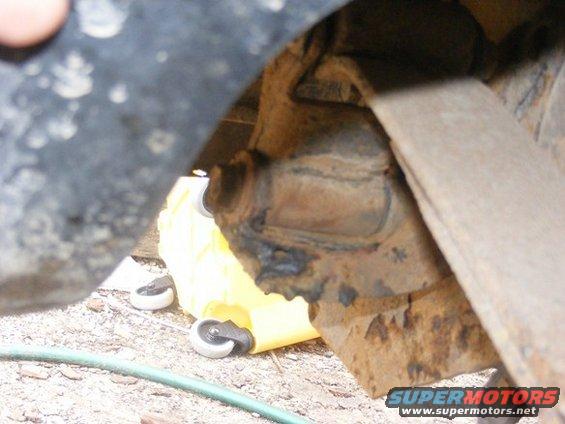 close-up of rusty vehicle suspension part with yellow jack stand wheels visible