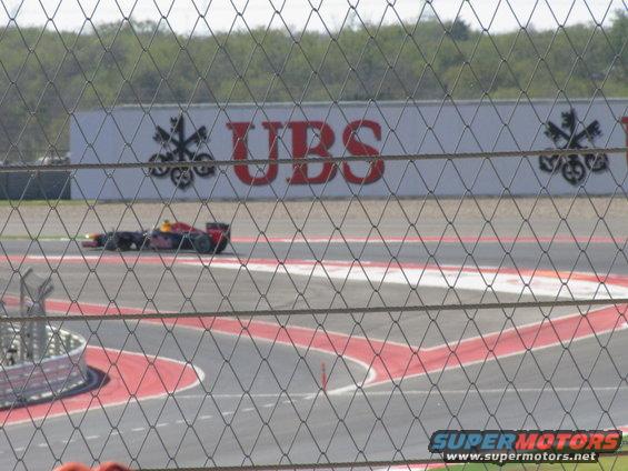 Formula 1 race car with red and yellow livery on a race track, with a UBS advertisement in the background