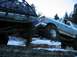 1988 Ford Bronco - Two heavily modified SUVs, including a 1988 Ford Bronco, tackle a challenging log obstacle in a snowy, wooded area.