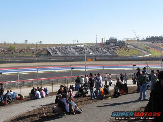 Race track with grandstands full of spectators and people sitting on the ground