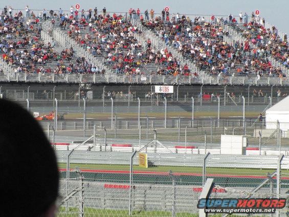 Orange race car on track with spectators in bleachers