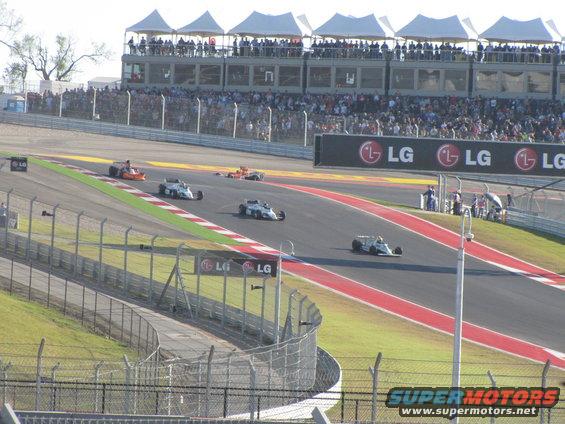 Open-wheel race cars speeding on a track with spectators in the stands and LG billboards