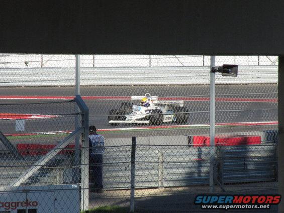 White and blue Formula 1 race car on track, side view