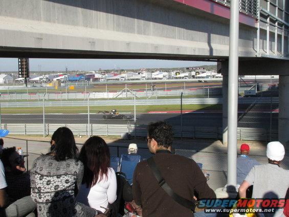 Race car on track with spectators in foreground under bridge