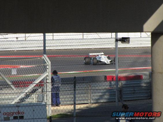 Race car on track, person in blue uniform watching