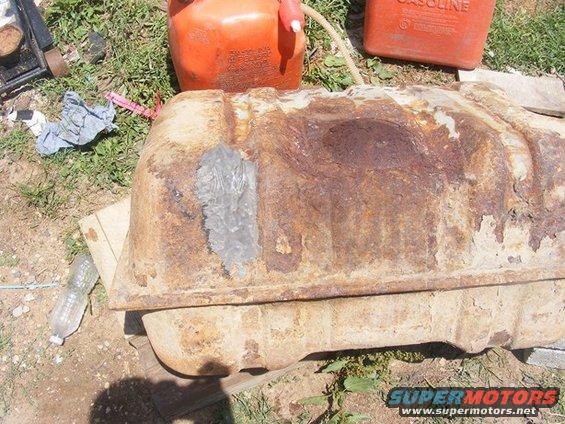 rusted fuel tank with a patch, next to gas cans