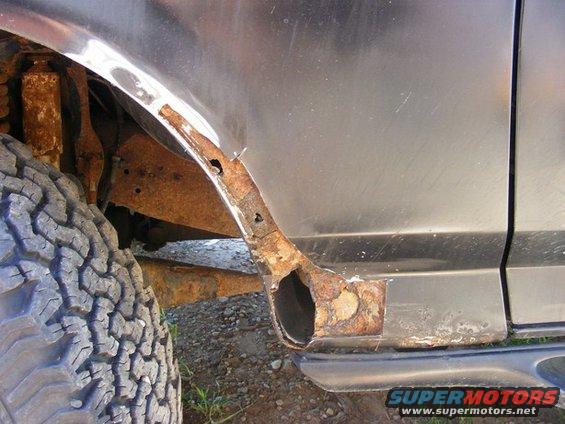 rusted out rear wheel well of a vehicle, showing significant corrosion on the fender and frame