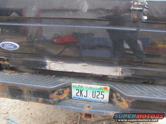 Black Ford tailgate with a Michigan license plate and visible rust damage
