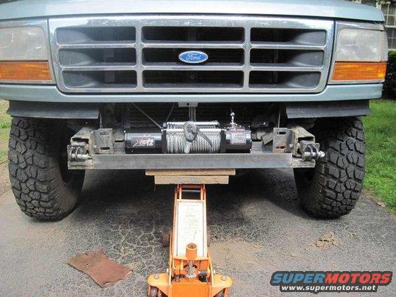 Green Ford Bronco front end with a winch mounted below the grille, supported by an orange hydraulic jack