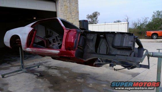 Car body on rotisserie, red and white primer, interior visible, orange truck in background