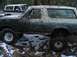 1988 Ford Bronco - A muddy Ford Bronco is seen off-road with another vehicle in the background.
