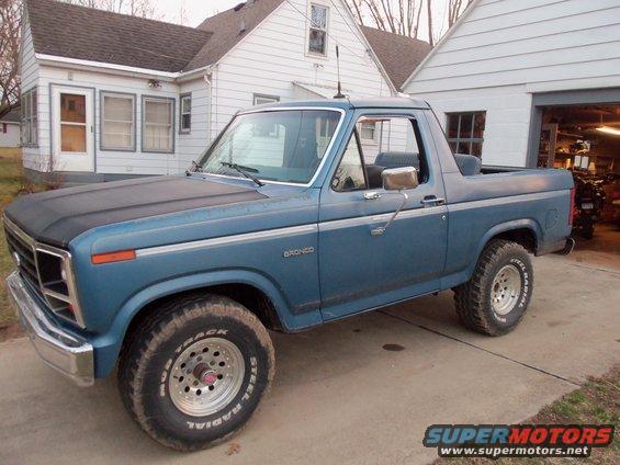 Blue Ford Bronco parked in driveway, front fender and side visible. Bronco script on door