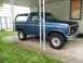 1985 Ford Bronco - A blue Ford Bronco with a white top is parked under a carport, showing its front quarter profile.