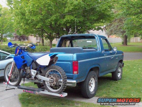 Blue 1985 Ford Bronco with dirt bike on rear carrier