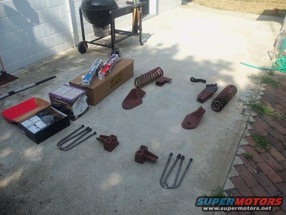 Vehicle suspension parts including U-bolts and springs laid out on concrete next to a grill