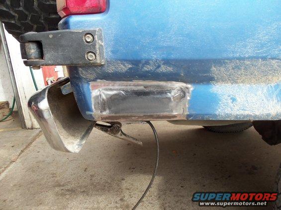 Blue SUV rear corner with chrome bumper section and welded metal repair on lower body panel