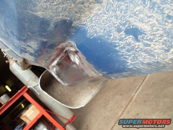 Close-up of a blue vehicle's undercarriage showing a freshly welded metal bracket and exhaust pipe