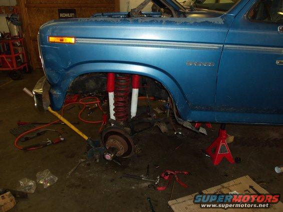 Blue Ford Bronco with red and white lifted suspension components, front wheel removed, in a garage
