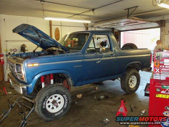1985 Ford Bronco in garage, hood open, red suspension components visible