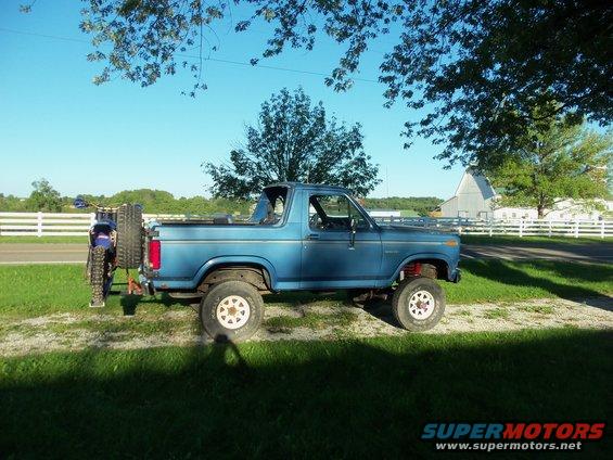 Blue 1985 Ford Bronco side view with dirt bike on rear carrier
