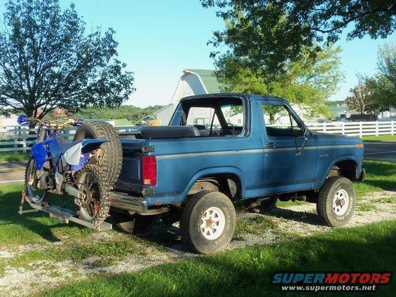 Blue Ford Bronco with a dirt bike mounted on a rear carrier rack