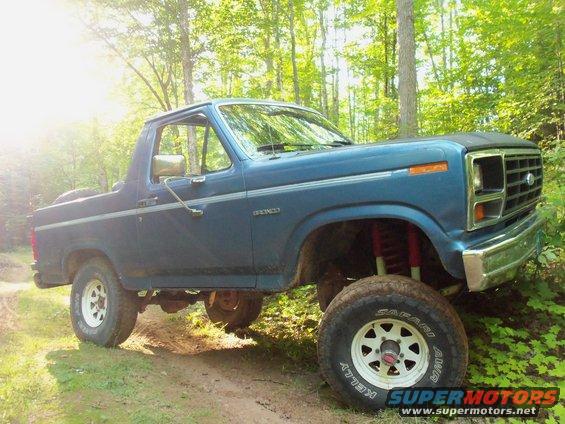 Blue lifted 1985 Ford Bronco parked on a dirt path in a wooded area
