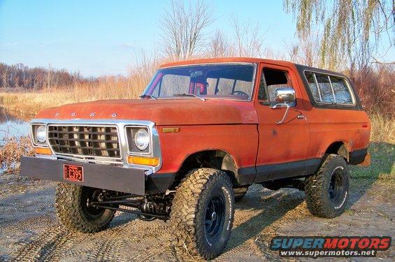 Orange 1978 Ford Bronco with a black bumper and large tires, parked outdoors on a dirt path