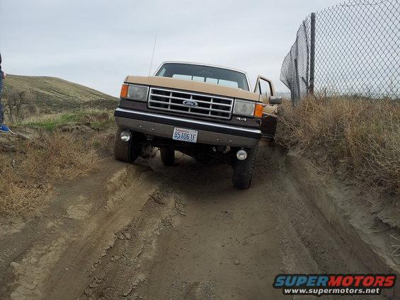 1987 Ford F-250 4x4 driving on a dirt track with open driver's door