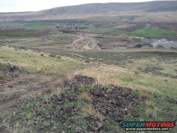 Overcast sky above a barren, hilly landscape with a dirt road leading to a construction site
