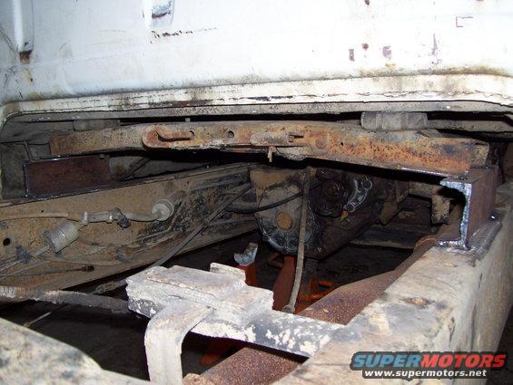 Underside of a white truck frame with rusty drivetrain components and a Supermotors.net watermark