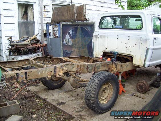 1972 Ford F-150 chassis on jack stands, white cab, rusty frame, large tires, in a yard