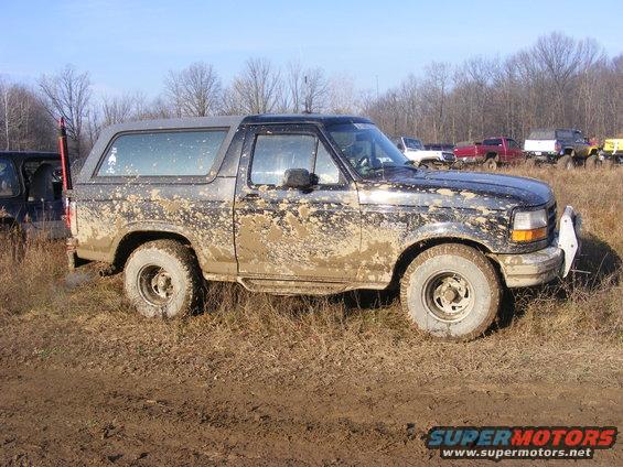 Mud-covered 1996 Ford Bronco parked in a muddy field with other vehicles in the background