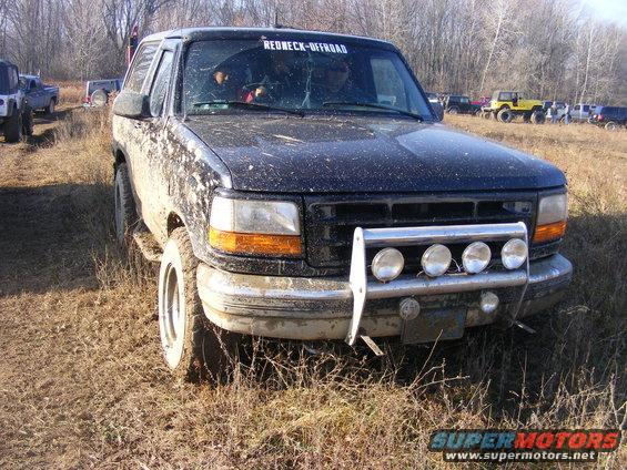 Mud-covered 1996 Ford Bronco parked in a grassy, muddy field with other vehicles in the background