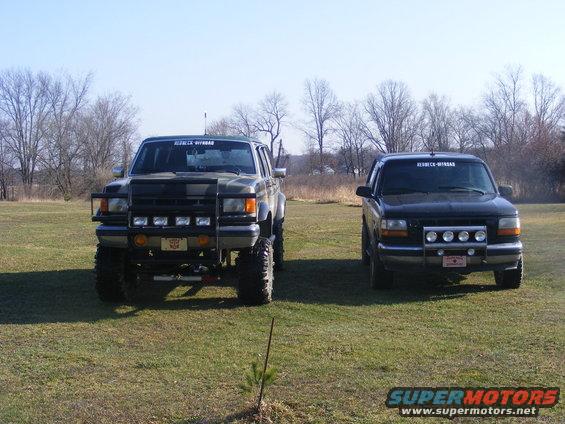 Two modified Ford SUVs parked on a grassy field under a clear sky