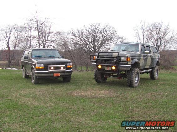 Two Ford Broncos parked on grass, one black, one camo with a bull bar