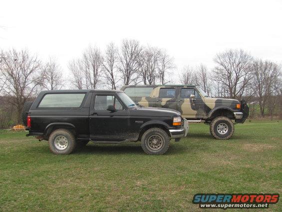 Black 1996 Ford Bronco parked next to a camouflage Ford F-Series truck