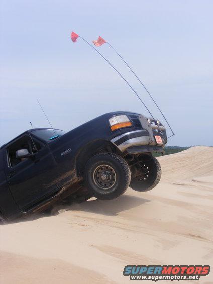 1996 Ford Bronco tilted on a sand dune with two orange flags on poles attached to the roof