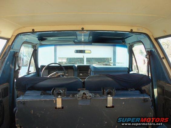 Interior view of a blue SUV, showing front seats, steering wheel, and rear storage box. Supermotors.net logo visible